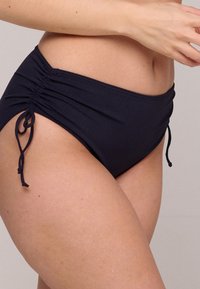 Marinblå högmidjad bikiniunderdel med rynkdetaljer och justerbara sidband. Slät, stretchig tyg ger en figurnära silhuett.
