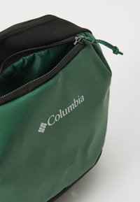 Bolsa Columbia verde con un acabado texturizado, cremallera negra y cordón. Presenta el logo en blanco en la parte frontal. Se abre desde la parte superior.