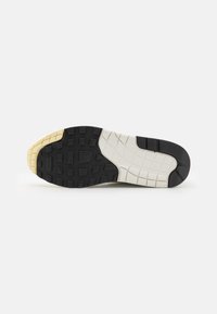 Sula av en sneaker med ett gummidesign i svart, vitt och krämfärgad. Har en texturerad yta med rutmönster och varumärkesdetalj.