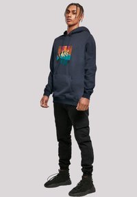 Navy hoodie with a front graphic of mountains and trees, featuring a front pocket and ribbed cuffs; paired with black cargo pants and boots.