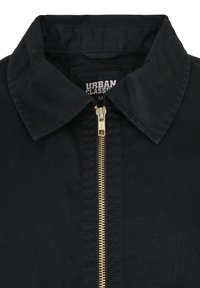 Musthave must kasukas kraejoonega, millel on kuldne lukk ja tekstuurne kangas. Sildil on kirjas "URBAN CLASSICS" valgete tähtedega.