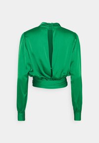 Blouse verte en satin à manches longues avec un col haut, détail de dos nu et taille froncée. Texture lisse avec une finition brillante.
