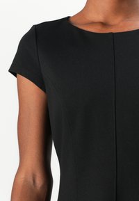 Robe noire ajustée en tissu doux, avec des manches courtes, un col rond et de subtils détails de couture sur les côtés.