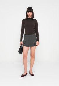 Langemouwenbruin top, grijze geplooide minirok, zwarte handtas en glanzende bordeauxrode schoenen. Eenvoudig ontwerp, zachte stof, casual uitstraling.
