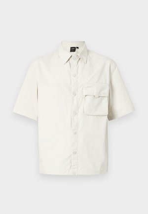 Kurzärmliges, kragenloses Hemd aus leichtem Beige Baumwollmaterial, mit einer Knopfleiste und einer aufgesetzten Brusttasche auf der linken Seite.