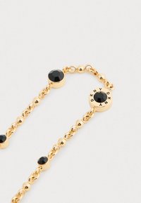 Goldkette Armband mit schwarzen facettierten Steinen und einem runden Anhänger, der mit "DKNY" um einen zentralen schwarzen Stein graviert ist.