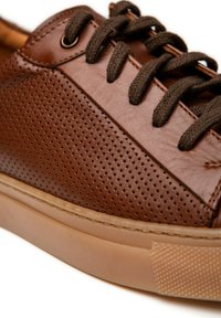 Brązowe skórzane trampki z perforowanymi detalami na cholewce, ciemnobrązowymi sznurowadłami oraz gumową podeszwą z teksturowanym wzorem.