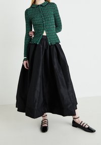 Groen gestreept, aansluitend longsleeve shirt met een kraag, gecombineerd met een volumineuze zwarte satijnen rok en zwarte strappy flats.