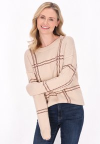 Beiger Pullover mit braunem Karomuster, rundem Ausschnitt und gerippten Bündchen. Getragen mit dunkelblauen Jeans, die eine lockere Passform und eine weiche Textur aufweisen.