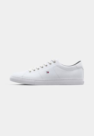 White sneakers with a smooth leather upper, six eyelets, subtle logo detail, and a flat rubber sole. Classic low-top design.