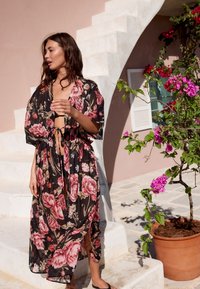 Svart kimono med blommönster i rosor, öppen fram, och knytning i midjan. Lätt tyg, korta ärmar och sidslitsar för rörelsefrihet.