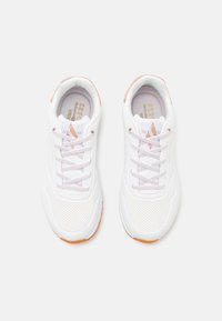 Une paire de baskets Skechers blanches avec une zone de orteils perforée, des lacets rose pâle et des accents beiges, vue de dessus sur un fond blanc.
