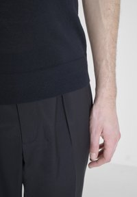 Maglione navy con orlo a coste, abbinato a pantaloni antracite. Il tessuto appare liscio, con una silhouette aderente e linee pulite.