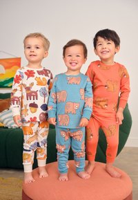 Tre børn har farverige pyjamasæt med dyreprint: beige (elge, egern), blågrøn (bjørne) og orange (egern). Blødt bomuldsstof.