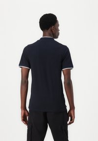 Marineblaues Poloshirt mit weißen Paspeln, kurzen Ärmeln und einem Kragen. Hergestellt aus weichem Stoff, bietet es eine taillierte Passform und minimale Designdetails.