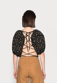 Blusa nera floreale con maniche a sbuffo e dettaglio della schiena con laccetti; presenta motivi gialli e verdi su uno sfondo scuro.
