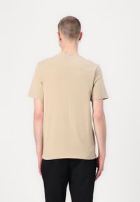 Beige színű, rövid ujjú póló, puha pamutból készült. Kerek nyakkivágással és egyenes hemmed van. Nincs rajta minta vagy látható fémrész.