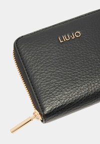 Portefeuille en cuir noir avec surface texturée, quincaillerie en métal doré et logo. Il dispose d'une fermeture éclair avec tirette en métal.