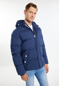 Marineblå dunjakke med hætte, frontlynlås, trykknapper og sideskaber. Blød tekstur og quiltet design for varme.
