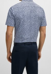 Košile s krátkým rukávem s námořnickým základem a bílým květinovým vzorem, která má zapínací límec a hladkou texturu látky.