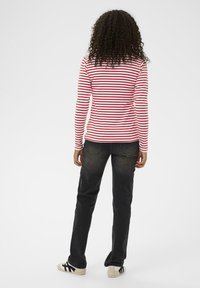 Červená a biela pruhovaná košeľa s dlhým rukávom skombinovaná s tmavými džínami a béžovými teniskami, zobrazená zozadu. Viditeľné kučeravé vlasy.