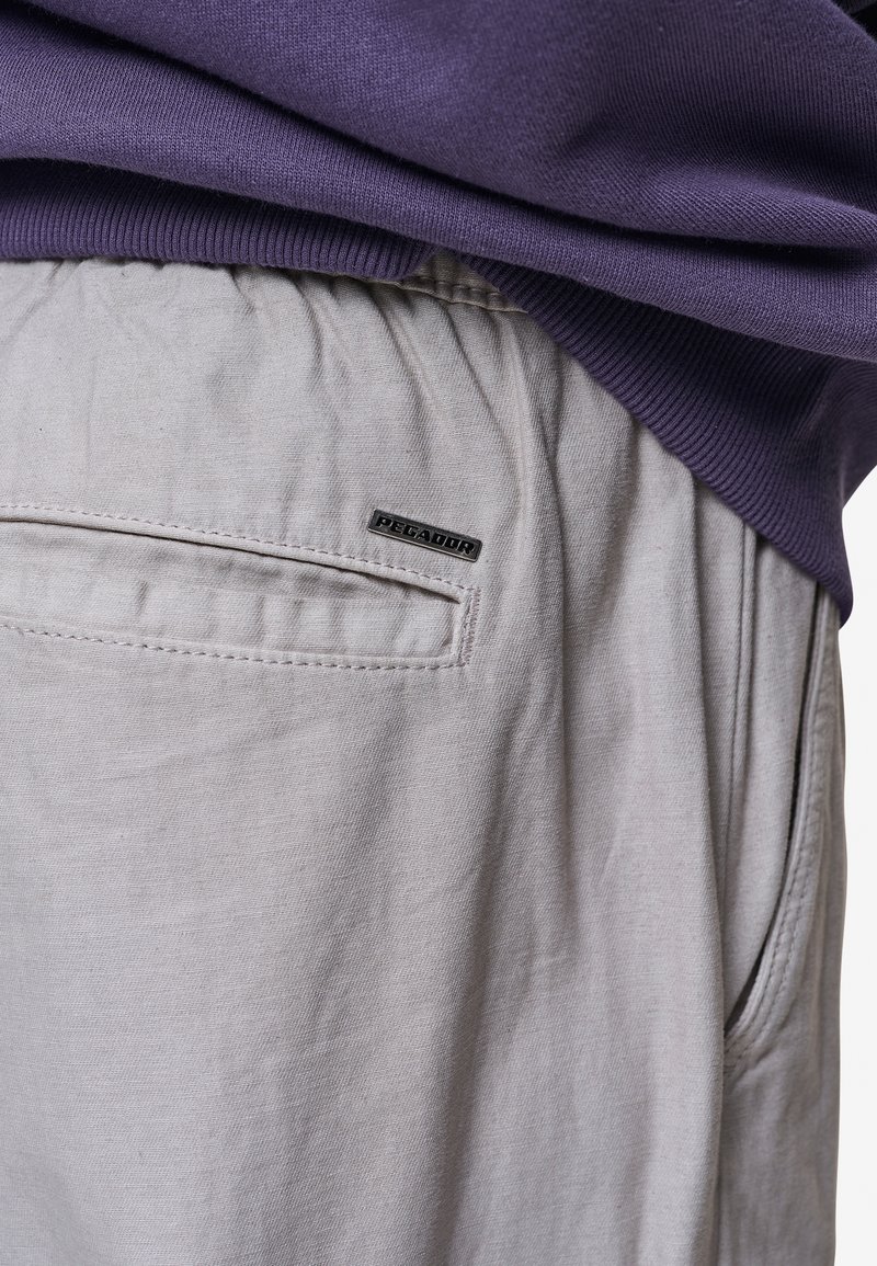 Jasnoszare spodnie z elastycznym paskiem w talii i tylną kieszenią z czarną metką "PEGA". Materiał jest gładki z delikatną teksturą.