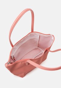 Rosa tote-väska gjord av texturerat material med en slät yta. Har en dragkedjeförslutning, dubbla handtag och en ljusrosa insida med fickor.