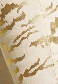 Patrón zigzag metálico dorado sobre una tela beige texturizada, con una superficie suave y lisa y un brillo sutil. Apta para tapicería o decoración.