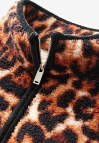 Veste en polaire avec imprimé léopard orange et noir, dotée d'une fermeture éclair et d'un col montant, mettant en avant une texture douce et un design moelleux.