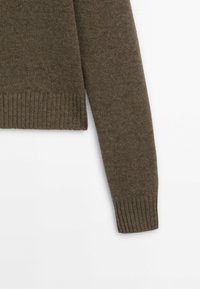 Maglione verde oliva lavorato a maglia con polsini e orlo a coste, realizzato in tessuto morbido. Si concentra sulla texture e sulla vestibilità senza motivi o accenti distinti.