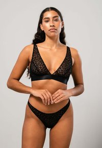 Schwarze Leopardenmuster-Bralette mit tiefem V-Ausschnitt und dünnen Trägern, kombiniert mit passendem Tanga. Durchsichtiges Material mit Satinakzenten.