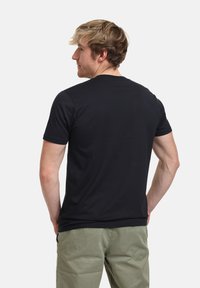 Černé tričko s krátkým rukávem vyrobené z bavlny, s klasickým kulatým výstřihem a jednoduchým designem, spojeno se světle zelenými kalhotami.