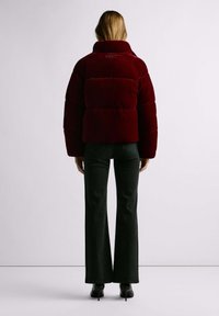 Rode velvet cropped pufferjas met een hoge kraag en pofmouwen, gecombineerd met wijde donkere jeans en zwarte schoenen met hoge hakken.