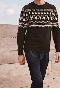 Suéter negro de punto con un patrón Fair Isle que presenta renos blancos, árboles y copos de nieve en el pecho, cuello redondo y acabado texturizado.