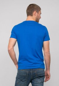 T-shirt en coton bleu avec un col rond, des manches courtes et une texture lisse. Porté avec un jean en denim bleu, montrant une coupe décontractée.