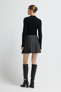 Zwarte geribbelde top met lange mouwen, gecombineerd met een grijze geplooide rok met krijtstrepen. Kniehoge zwarte leren laarzen met hakken en gouden accenten.