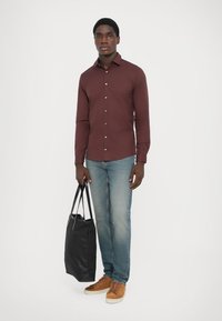 Mörkröd skjorta med knappar, ljusblå jeans, bruna sneakers, hållandes en svart tote-väska. Slät tyg, åtsittande design, minimalistisk stil.