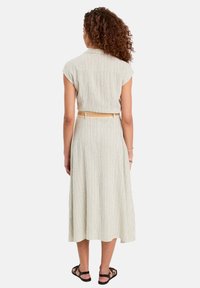 Robe midi à rayures vert clair avec des manches courtes, taille cintrée et ceinture tissée. Le tissu présente une texture naturelle et un drapé doux.