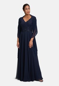 Marineblå aftenkjole med blonde overdel, V-udskæring og fløjlsagtig chiffon nederdel, ledsaget af en gennemsigtig matchende sjal.