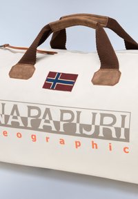 Hvid duffelbag med brune stofhåndtag og læderdetaljer. Har et norsk flag lap og "NAPAPIJRI" logo i grå og orange.
