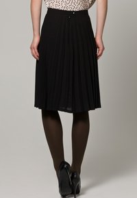 Svart plisserad midikjol i strukturerat tyg med figursydd midja och en subtil glans. Matchas med svarta högklackade skor och ogenomskinliga strumpbyxor.