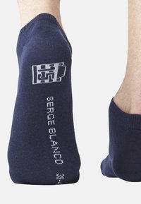 Chaussettes chevilles bleu marine en tissu doux, présentant un logo blanc et le texte "SERGE BLANCO" sur le côté. Texture lisse et forme ajustée.