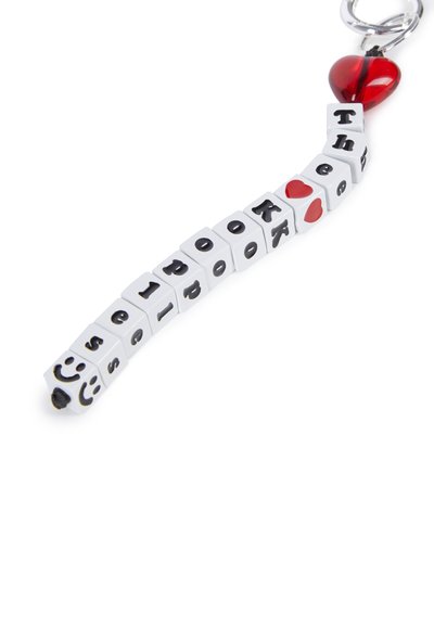 Witte plastic sleutelhanger met zwarte letters die "The Look" spellen, voorzien van een rode hartbedel en een zwarte glimlachende gezicht aan het ene uiteinde.
