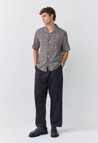 Camicia a maniche corte con bottoni, con motivo a griglia multicolore. Abbinata a pantaloni neri larghi e scarpe scure con lacci. Tessuto dalla texture liscia.