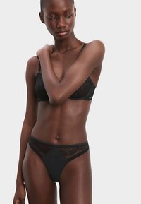 Ensemble de lingerie noire en dentelle et maille comprenant un soutien-gorge avec un délicat bord en dentelle et un string assorti avec des accents en dentelle, texture de tissu lisse.