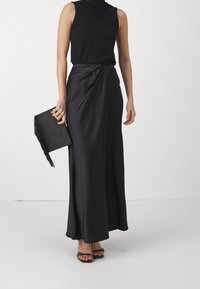 Czarna top bez rękawów w połączeniu z długą, czarną satynową spódnicą, z detalem skrętu, uzupełniona czarną torebką kopertową z frędzlami.