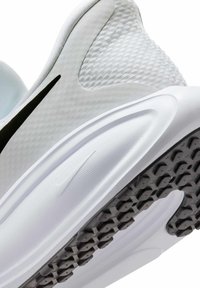 Chaussure de sport blanche avec tige en mesh texturé, logo Nike swoosh noir, et une semelle extérieure hexagonale noire visible.