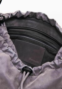 Torba na navlačenje od mekog sivog materijala; sadrži teksturiranu površinu, crnu patentnu vrećicu i utisnuti logotip na unutarnjoj oznaci.