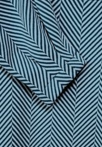 Vävt tyg med ett blått och vitt chevronmönster. Texturen är slät, med diagonala ränder som skapar en dynamisk visuell effekt.