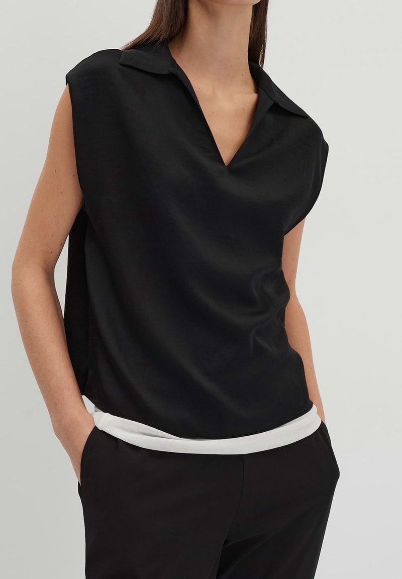 Haut noir sans manches avec un col en V et un col, présentant une texture douce et lisse ainsi qu'un ourlet blanc contrastant en bas.